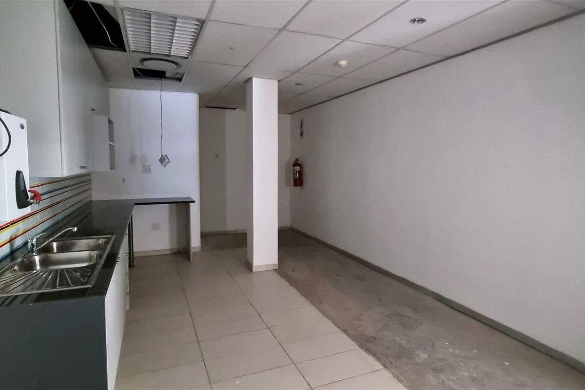 A functional office kitchenette area featuring a stainless steel sink, built-in cabinetry, and tiled flooring, currently requiring maintenance and ceiling repairs.