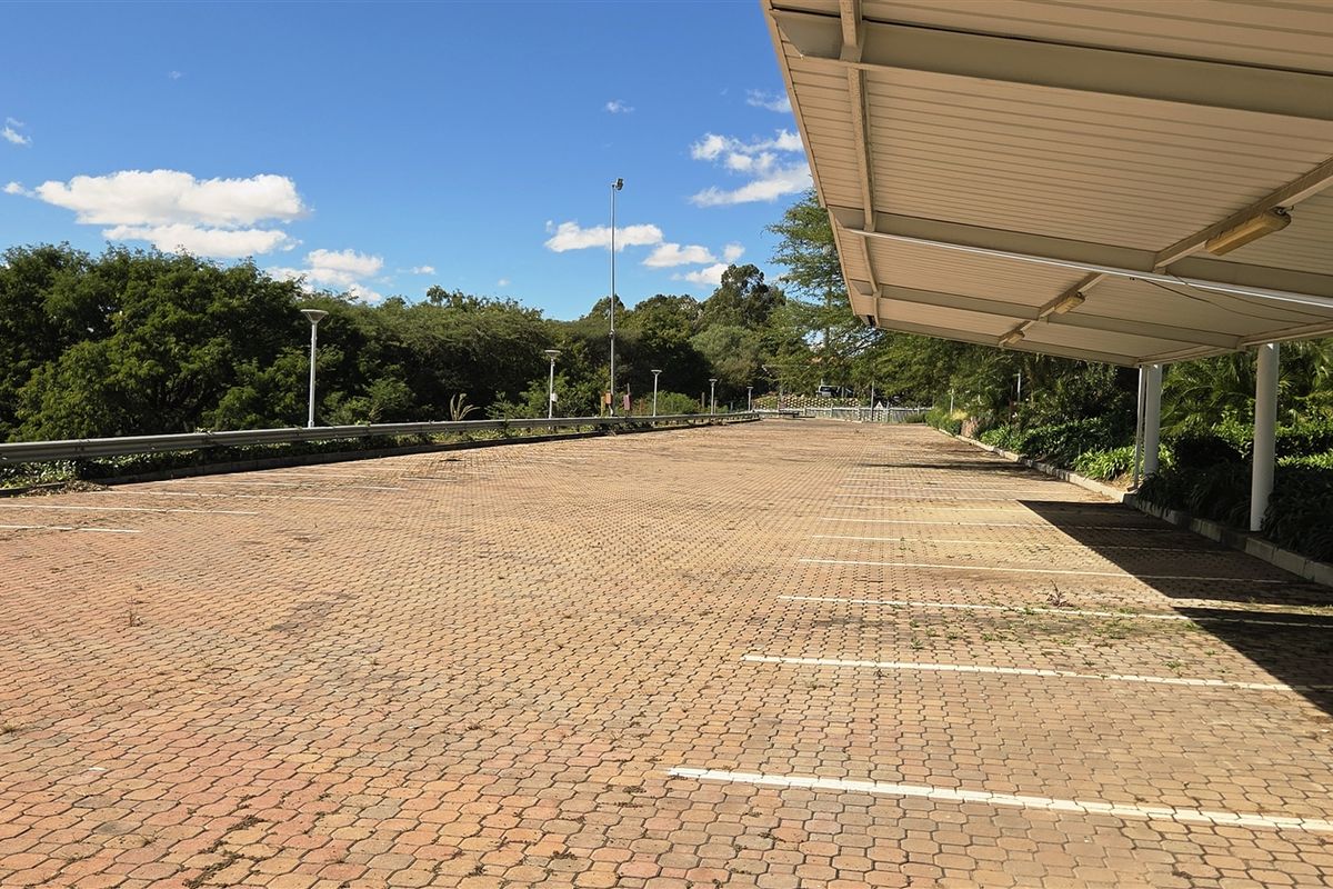 An outdoor paved parking area featuring a covered section with overhead lighting, providing ample space for multiple vehicles.