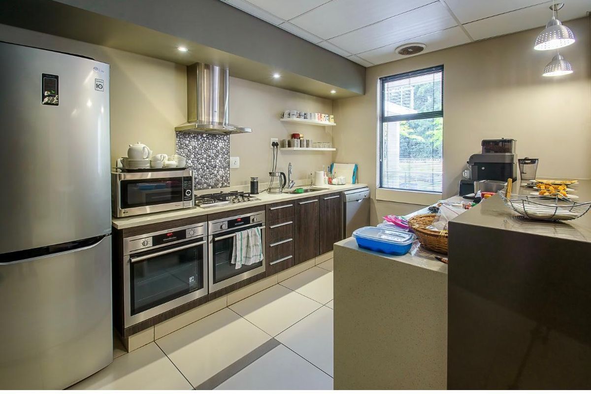 Modern office kitchen featuring dark wood cabinetry, stone countertops, dual built-in ovens, gas hob, and tiled flooring.