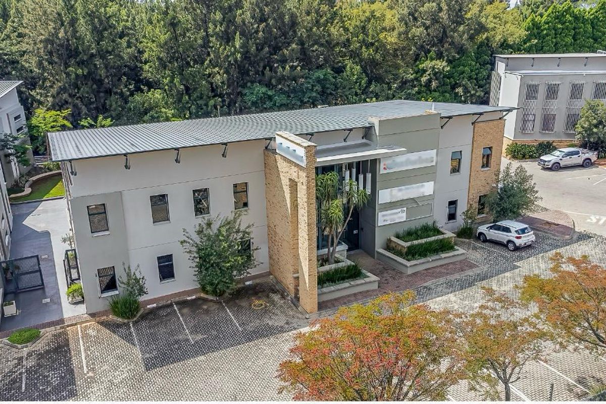 Aerial view of a modern office building featuring a metal roof, brick accents, and a paved parking area with integrated landscaping.