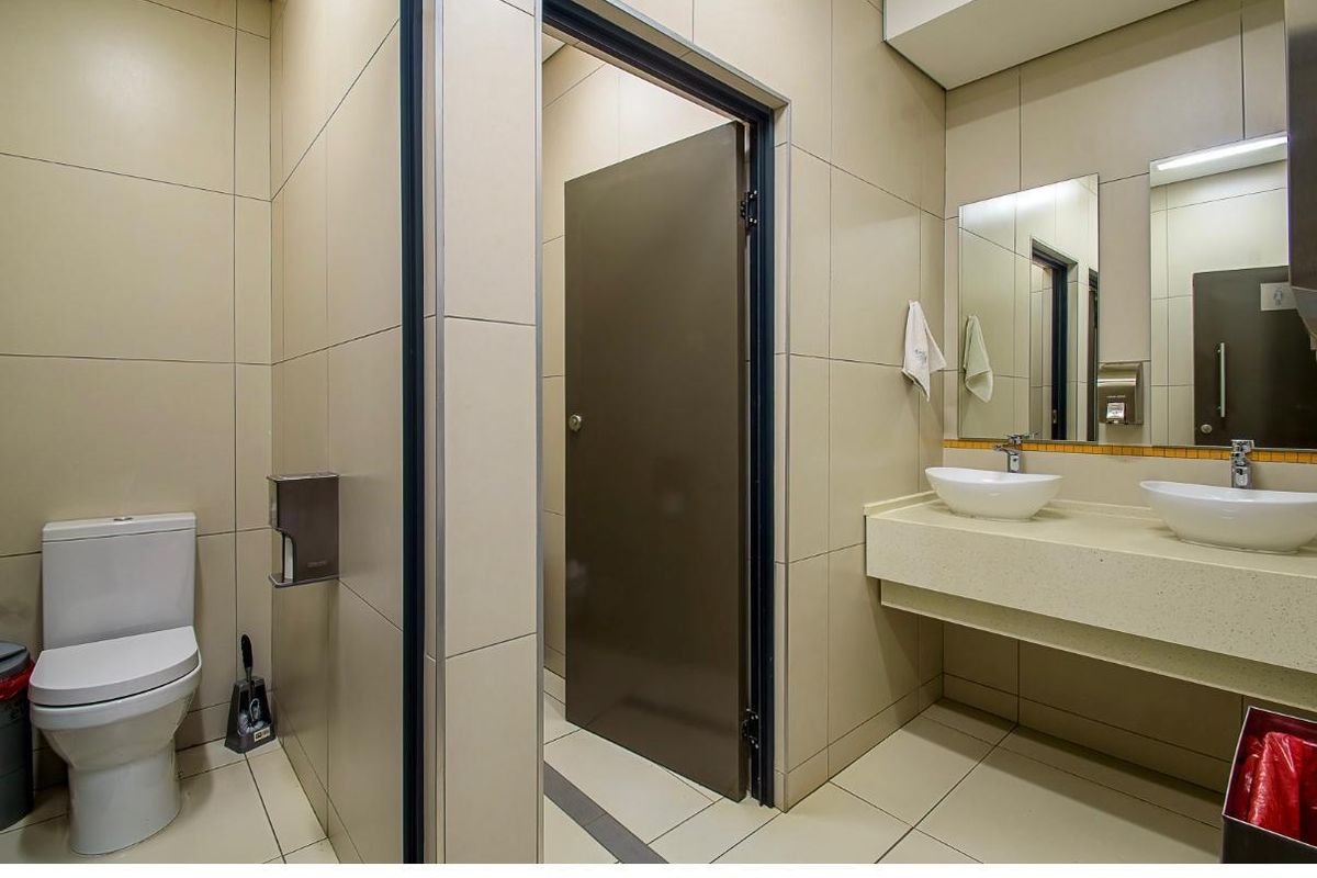 A modern office bathroom featuring dual vessel sinks, a built-in vanity countertop, and neutral floor-to-ceiling wall tiling.