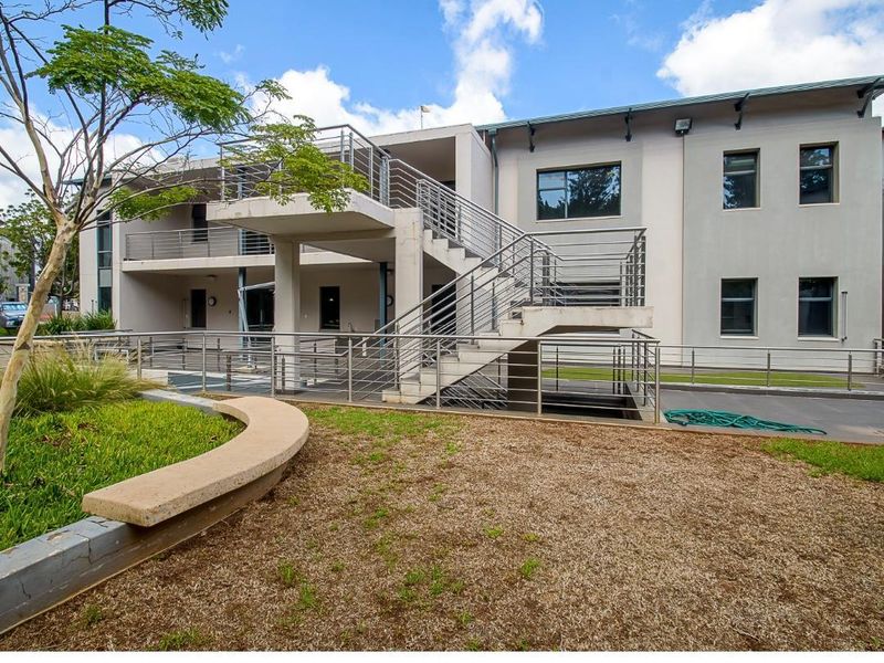 Rear view of the office building featuring an external concrete staircase with stainless steel railings, paved courtyard area, and landscaped garden beds.