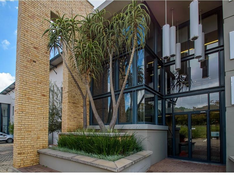 Modern office building entrance featuring a striking face brick facade, expansive glass curtain wall, and a landscaped built-in planter box.