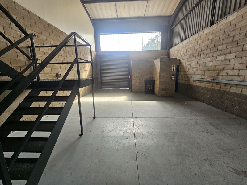 Spacious industrial utility area featuring concrete flooring, exposed brick walls, a metal staircase, and a large roller shutter door for easy access.