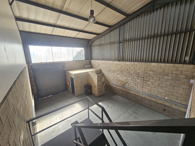 Industrial utility space featuring high ceilings, exposed brick walls, a roller shutter door, and metal staircase access.