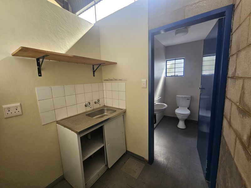 Utility area featuring a stainless steel sink with tiled splashback, adjacent to a small private restroom with a toilet and basin.