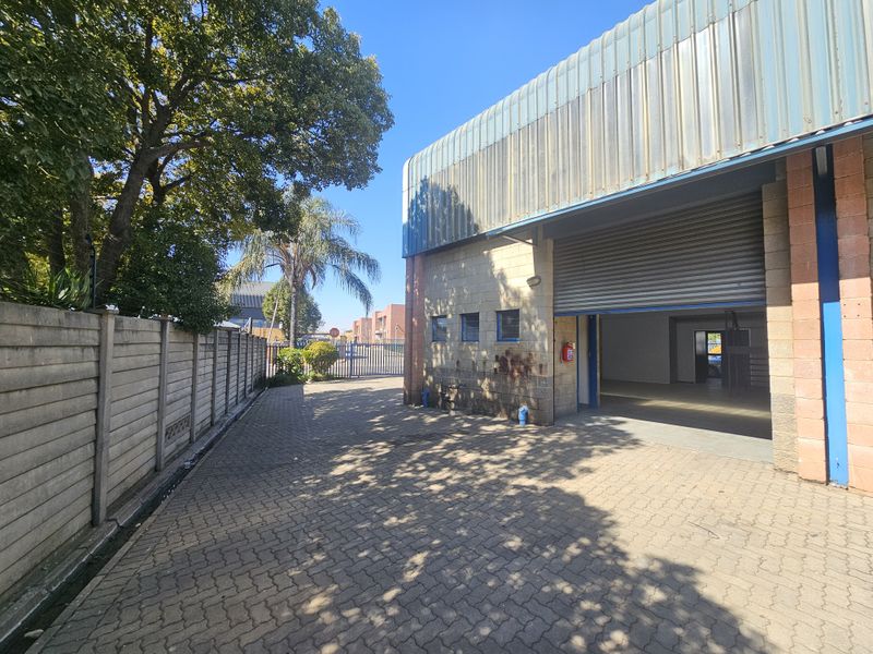 Industrial property exterior featuring a paved driveway, roller shutter door access, and precast concrete boundary walling.