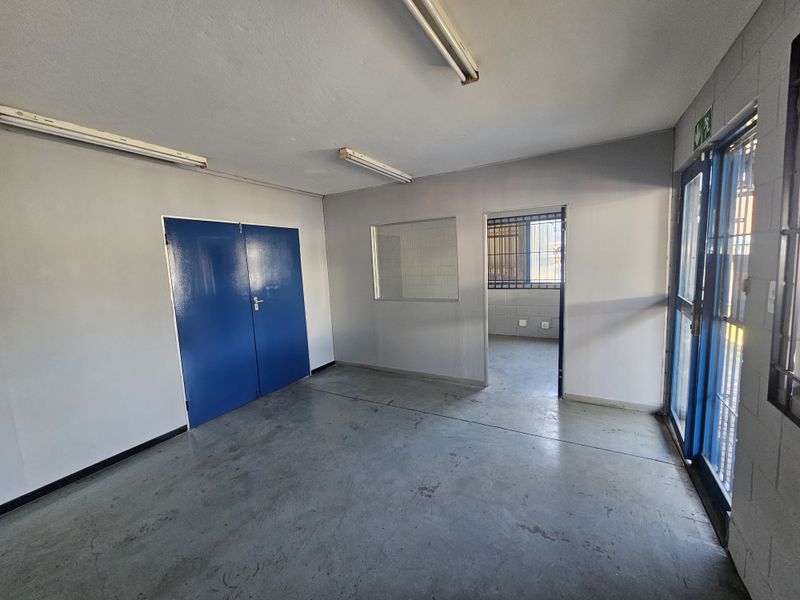 Empty industrial office space featuring concrete flooring, fluorescent lighting, and security bars on windows and doors.