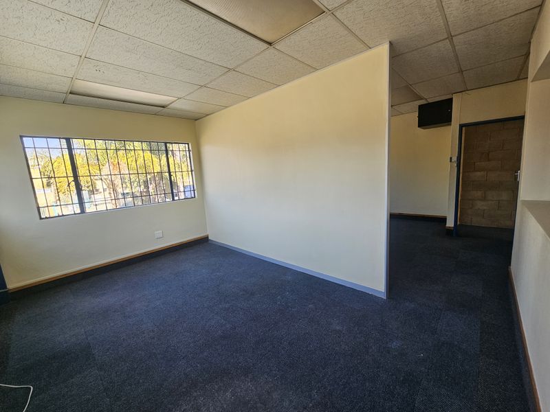 An empty office space featuring a suspended ceiling, security bars on the window, and carpeted flooring, suitable for a professional workspace.