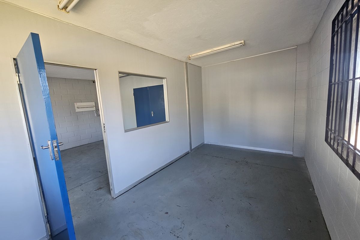 An empty industrial office space featuring painted blockwork walls, concrete flooring, security bars on windows, and fluorescent lighting.