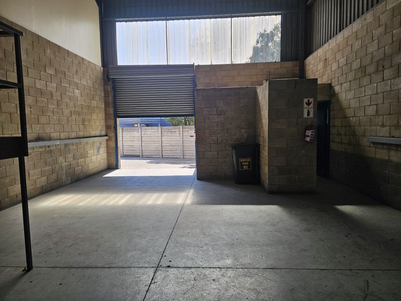Industrial garage space featuring concrete flooring, exposed blockwork walls, and a large roller shutter door providing access to the exterior.