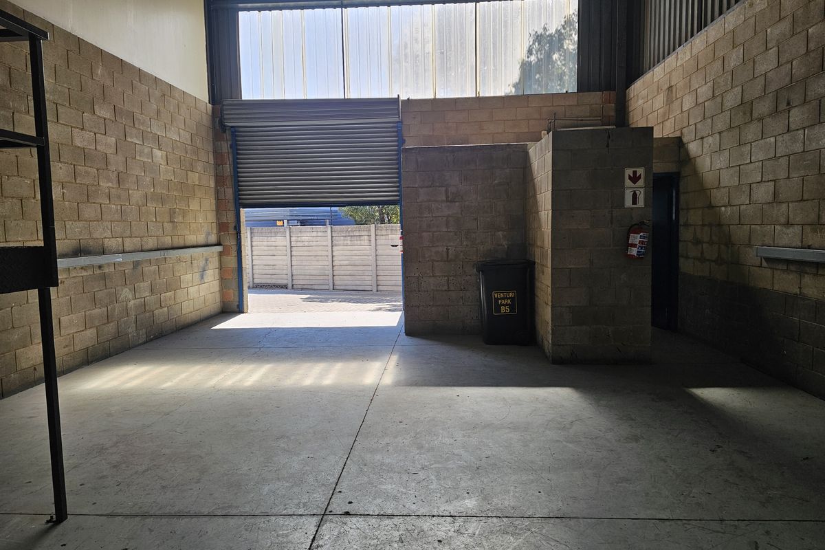 Industrial garage space featuring concrete flooring, exposed blockwork walls, and a large roller shutter door providing access to the exterior.