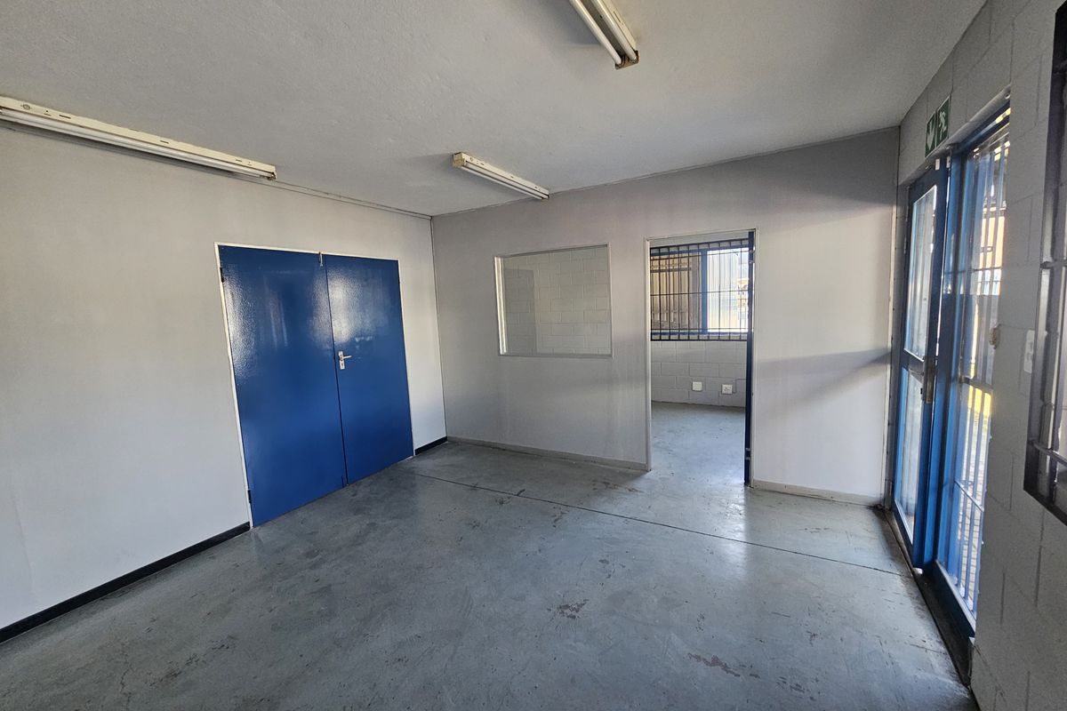 Empty industrial office space featuring concrete flooring, fluorescent lighting, and security bars on windows and doors.