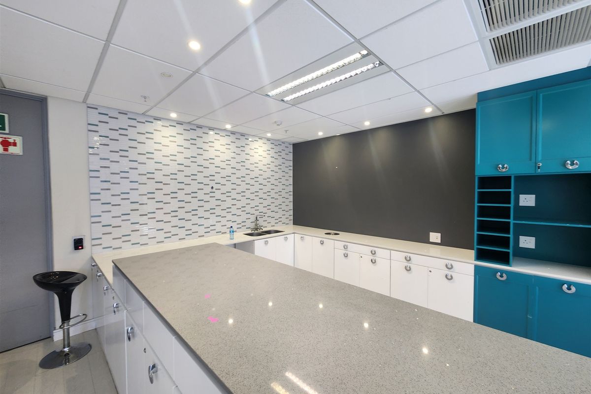 Modern office kitchenette featuring stone countertops, built-in cabinetry, a stainless steel sink, and a decorative tiled backsplash.