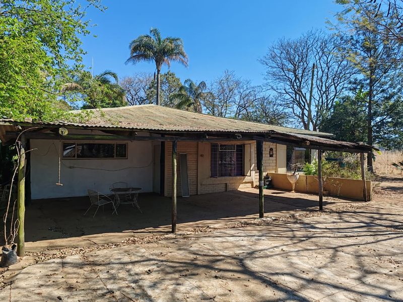 Rear view of a farm property featuring a large covered patio area with a corrugated metal roof and brick exterior walls.