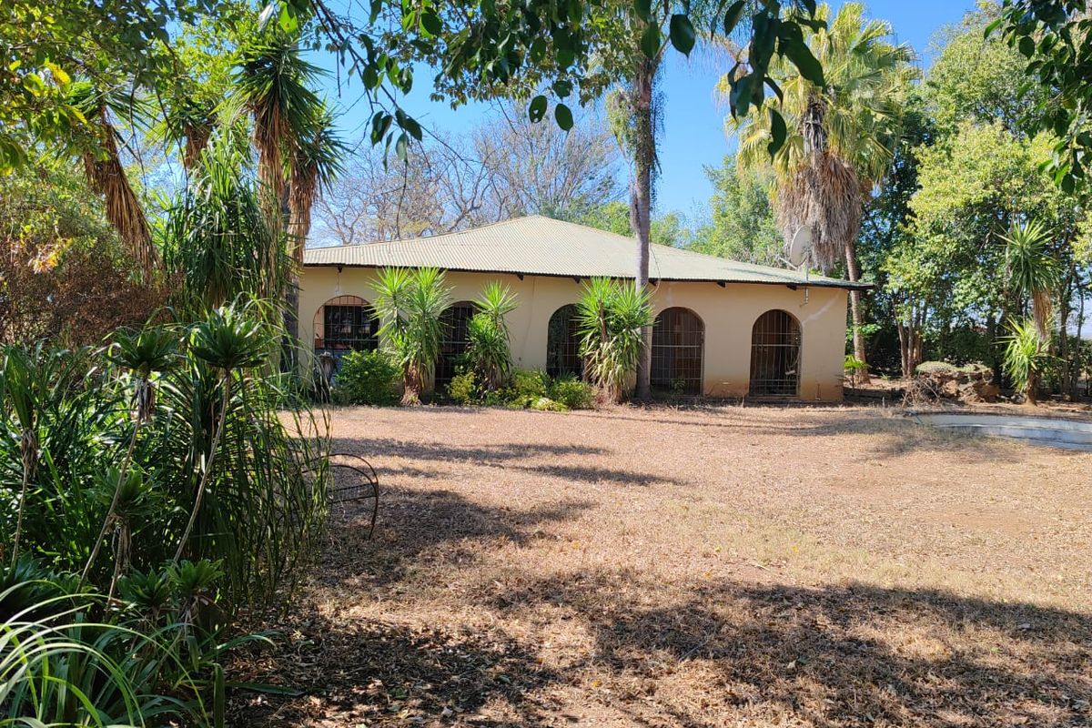 Rear view of a farm-style dwelling featuring an arched veranda, metal roofing, and established garden surroundings.