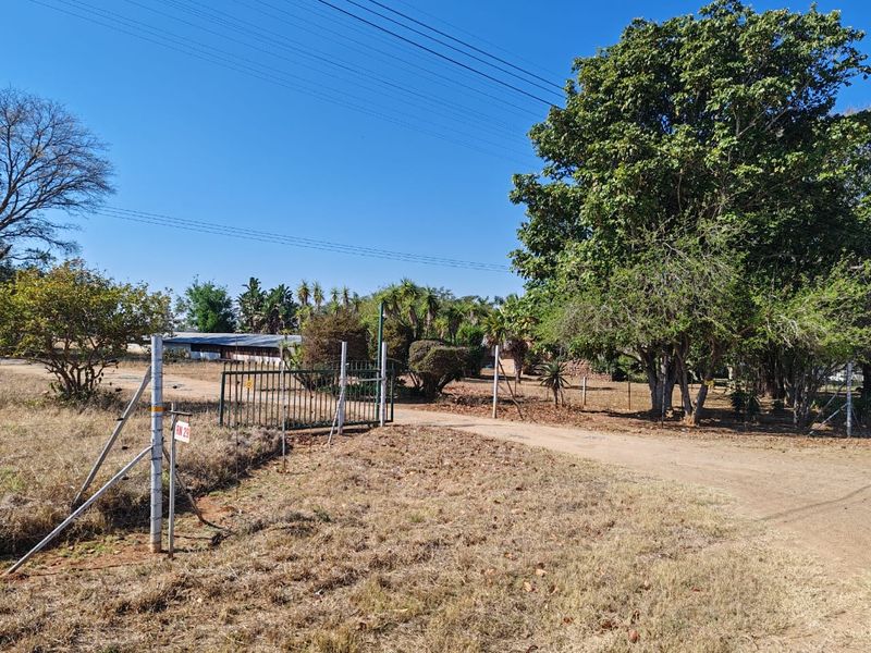A view of the property entrance featuring a metal gate, wire fencing, and a dirt driveway surrounded by mature trees on a farm.