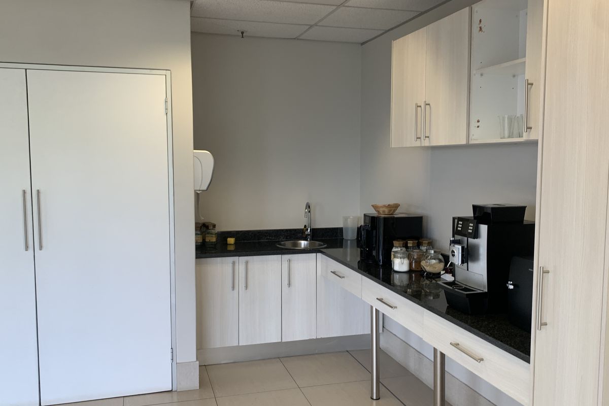 A functional kitchenette area featuring light wood-grain cabinetry, dark granite countertops, a stainless steel sink, and a suspended ceiling.