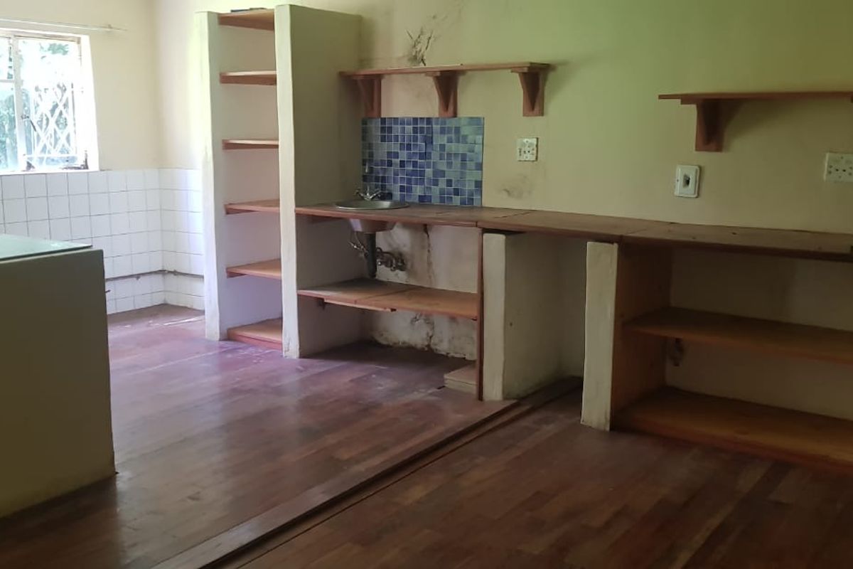 A dated kitchen area featuring built-in wooden shelving, a sink, and tiled splashbacks, requiring renovation to update the finishes and address wall damage.