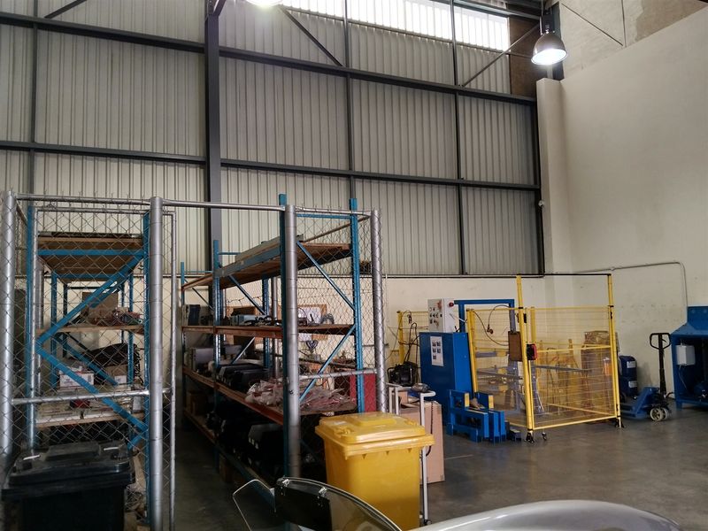 Industrial warehouse space featuring high ceilings, steel portal frame construction, concrete flooring, and integrated safety fencing for storage and operational areas.