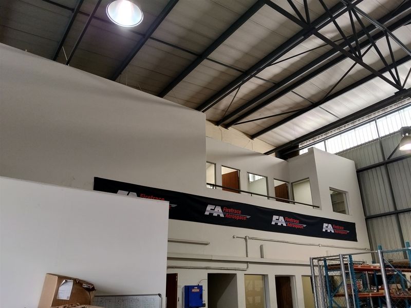 Industrial warehouse space featuring a high-bay ceiling with exposed steel trusses and a mezzanine level with integrated office partitioning.