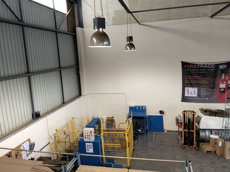 High-ceiling industrial utility space featuring exposed steel structure, metal wall cladding, concrete flooring, and industrial pendant lighting.