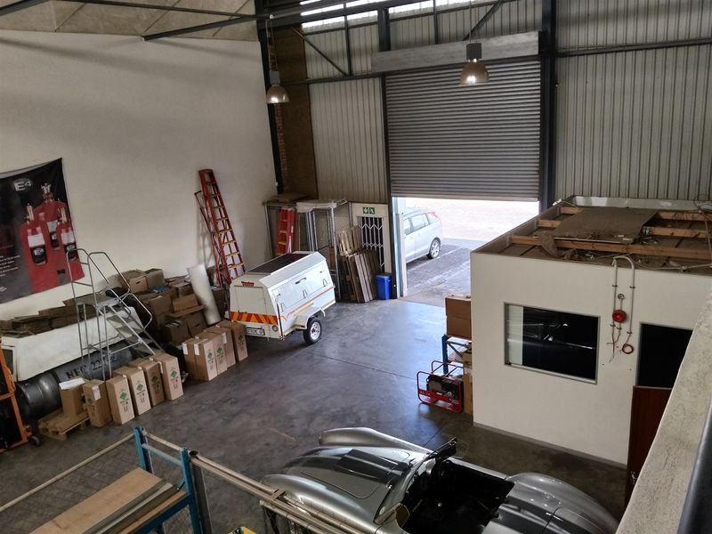 Spacious industrial warehouse unit featuring a large roller shutter door, high ceilings, concrete flooring, and an integrated mezzanine office area.