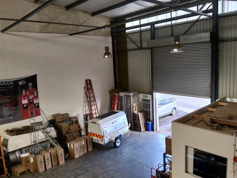 Spacious industrial warehouse unit featuring high ceilings with exposed steel trusses, concrete flooring, and a large roller shutter door for vehicle access.