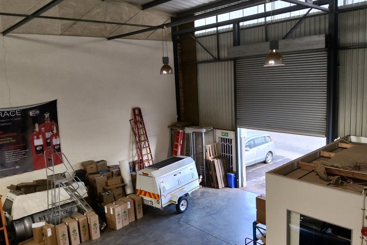 Spacious industrial warehouse unit featuring high ceilings with exposed steel trusses, concrete flooring, and a large roller shutter door for vehicle access.