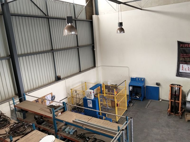 High-ceiling industrial utility space featuring exposed steel trusses, corrugated metal wall cladding, concrete flooring, and industrial pendant lighting.