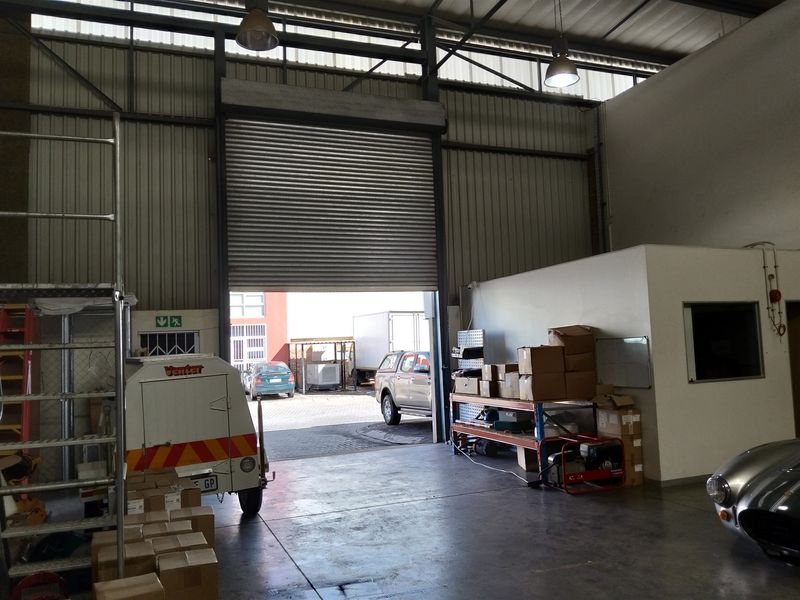 Spacious industrial warehouse or garage area featuring high ceilings, concrete flooring, and a large roller shutter door for vehicle access.