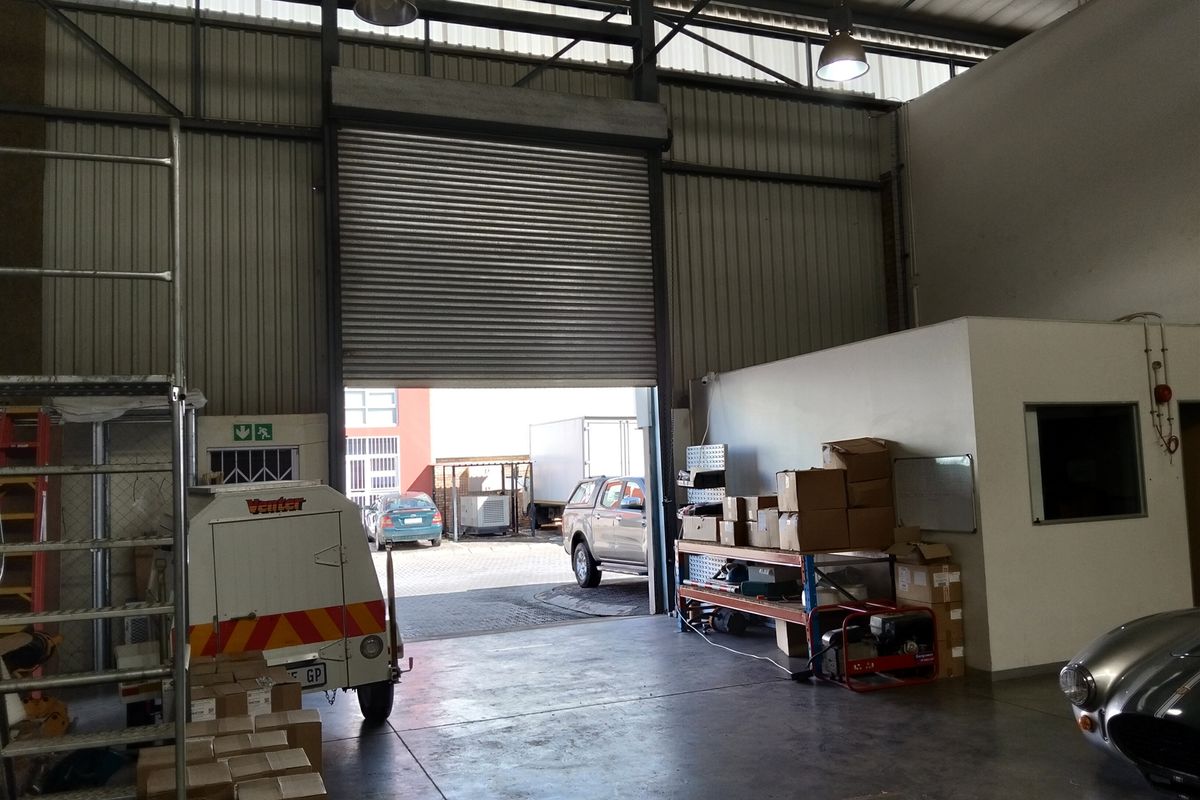 Spacious industrial warehouse or garage area featuring high ceilings, concrete flooring, and a large roller shutter door for vehicle access.