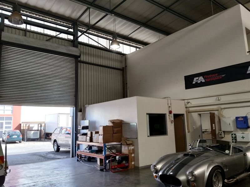 Spacious industrial garage featuring a large roller shutter door, high ceilings with exposed steel trusses, and an integrated internal office space.