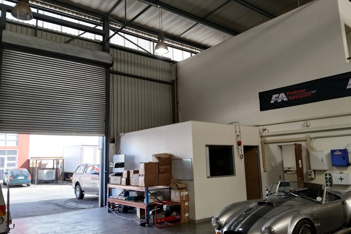Spacious industrial garage featuring a large roller shutter door, high ceilings with exposed steel trusses, and an integrated internal office space.