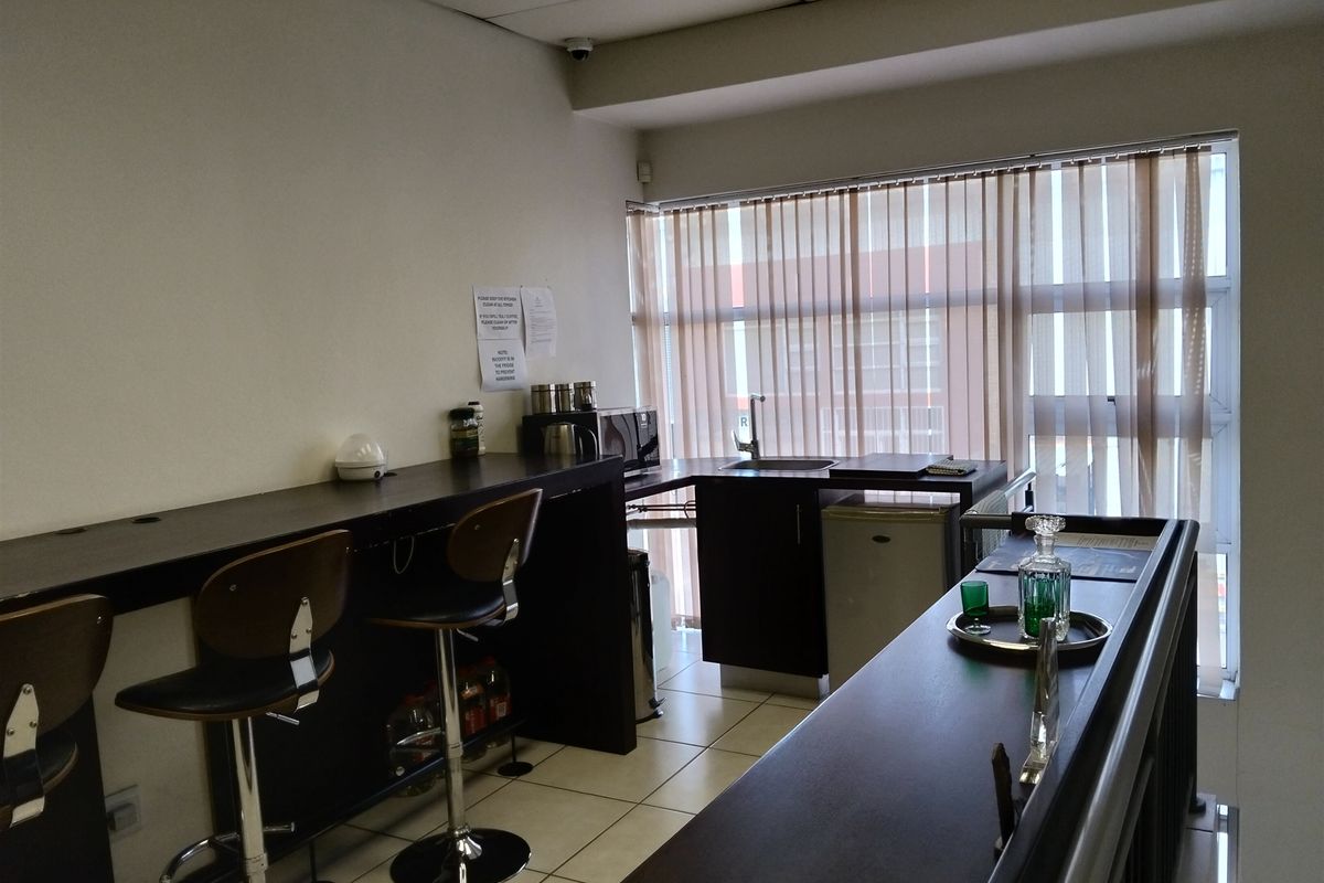 A functional kitchenette area featuring a built-in counter, stainless steel sink, and tiled flooring, suitable for office or industrial breakroom use.