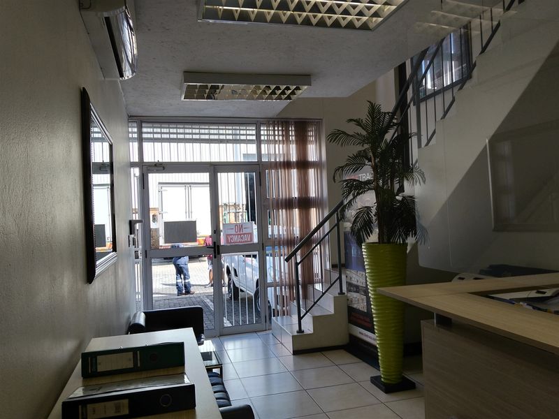 Industrial office entrance area featuring tiled flooring, a staircase, and a secure glass-panelled entrance door.
