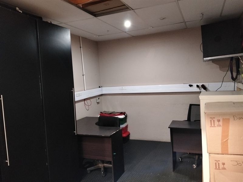 A small office space featuring rubber flooring, surface-mounted electrical trunking, and a suspended ceiling with a missing tile.