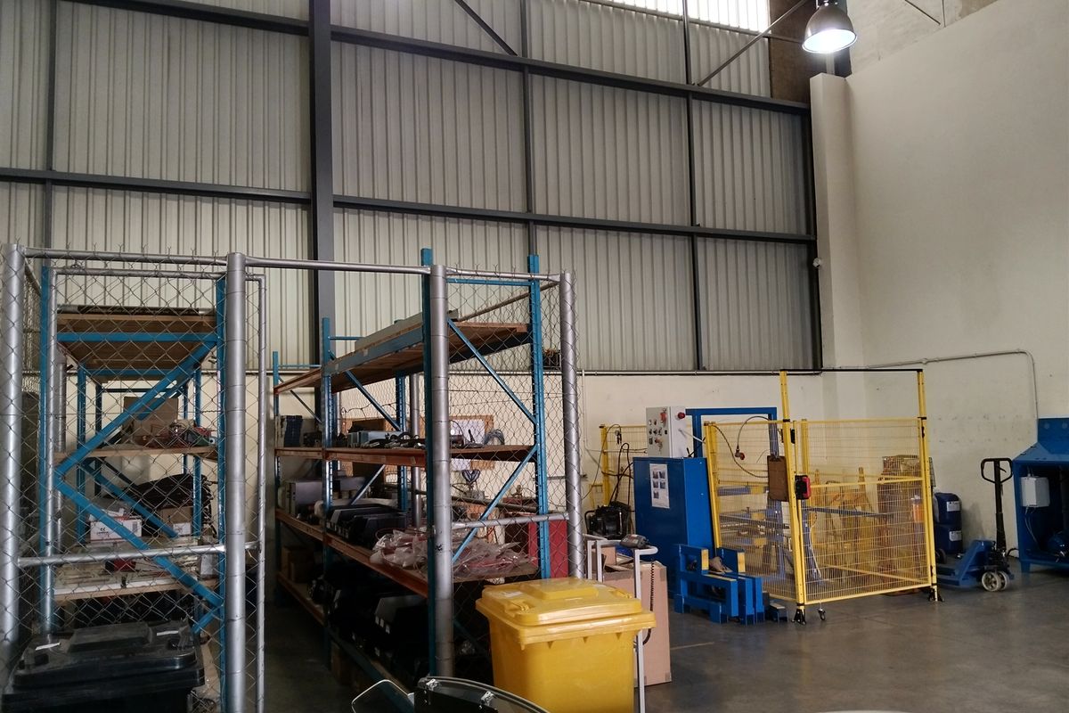 Industrial warehouse space featuring high ceilings, steel portal frame construction, concrete flooring, and integrated safety fencing for storage and operational areas.
