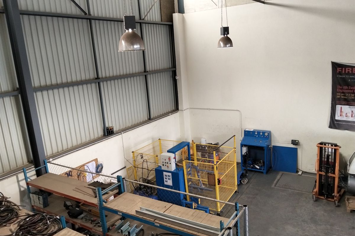 High-ceiling industrial utility space featuring exposed steel trusses, corrugated metal wall cladding, concrete flooring, and industrial pendant lighting.