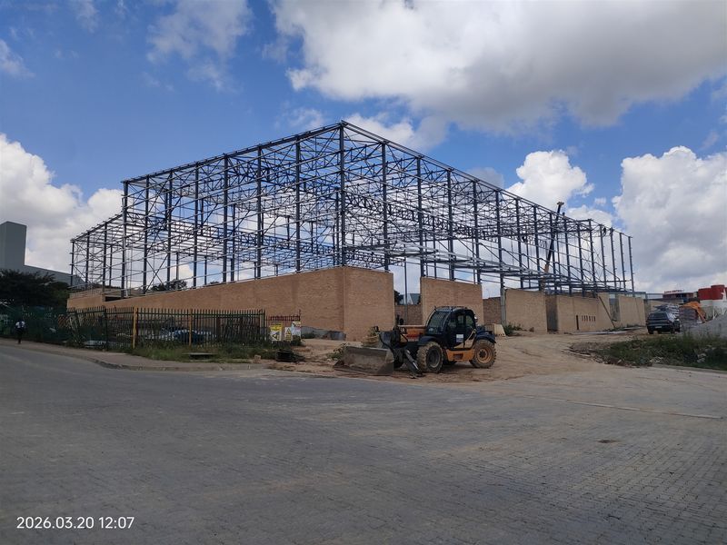 Industrial property under construction featuring a steel portal frame structure and brick masonry walls on a development site.