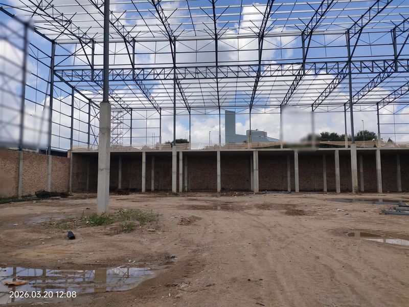 An industrial warehouse shell featuring a steel portal frame structure, concrete columns, and exposed brickwork, currently in an unfinished construction state.
