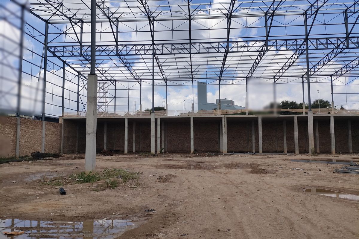 An industrial warehouse shell featuring a steel portal frame structure, concrete columns, and exposed brickwork, currently in an unfinished construction state.