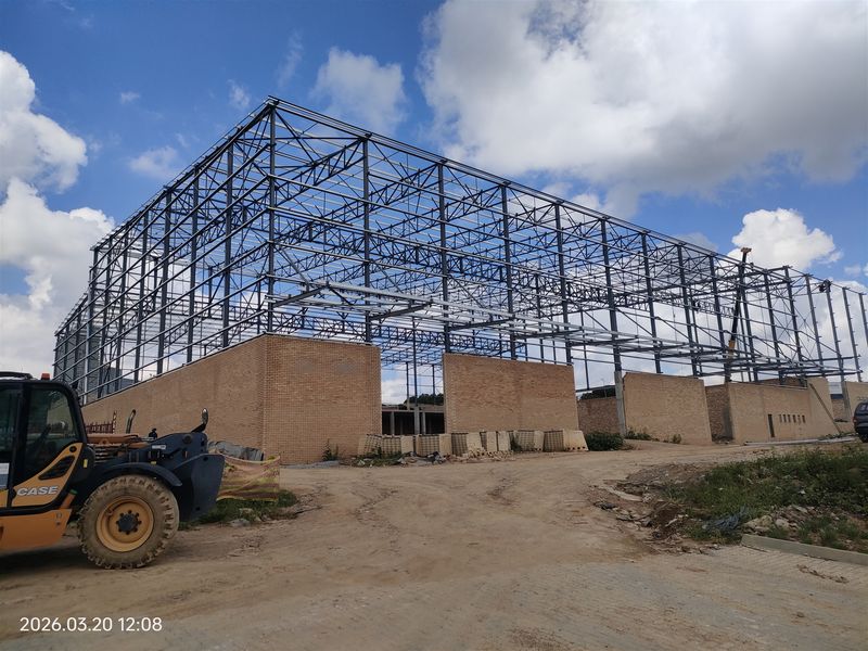 A construction site view showing the steel portal frame and face brick walls of an industrial building currently under development.