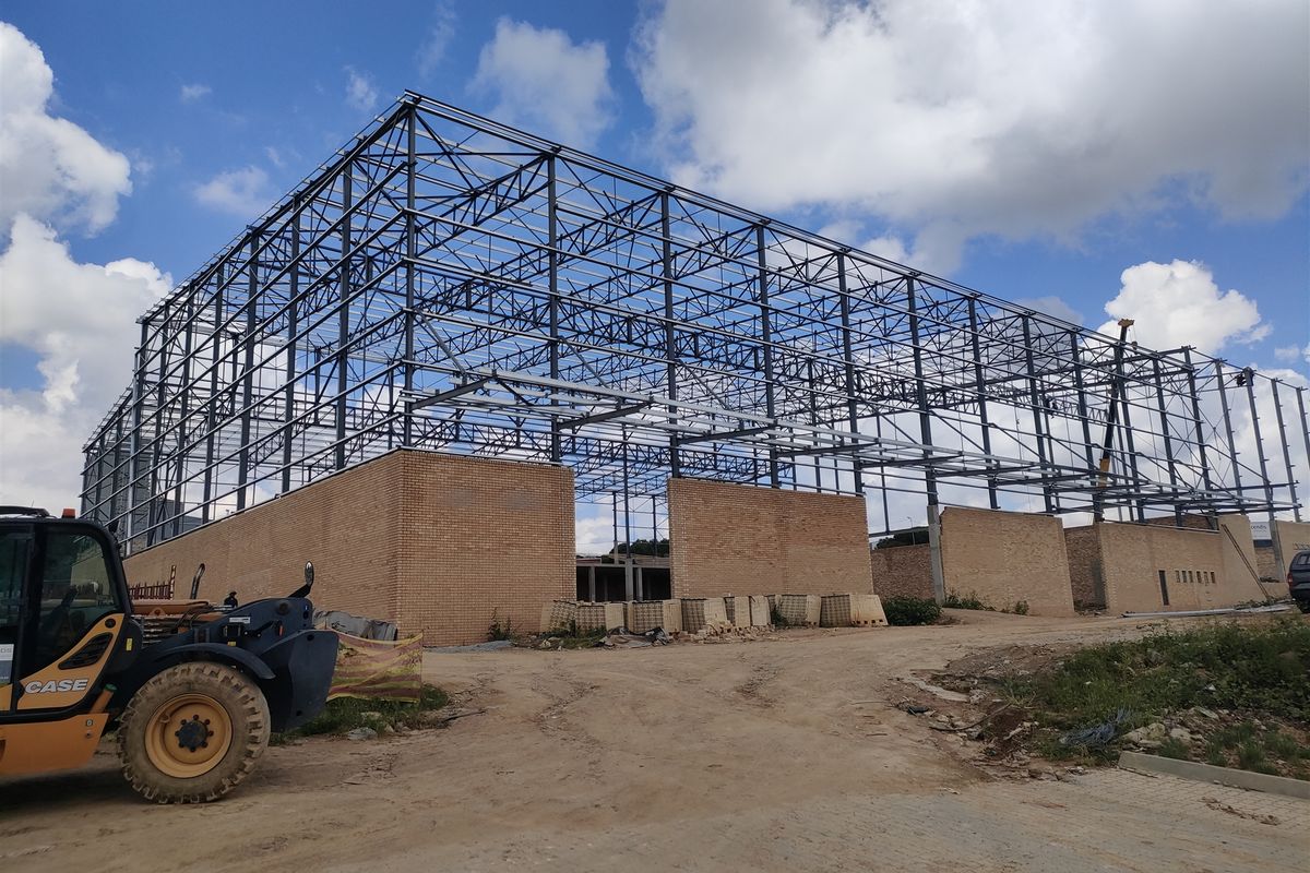 A construction site view showing the steel portal frame and face brick walls of an industrial building currently under development.