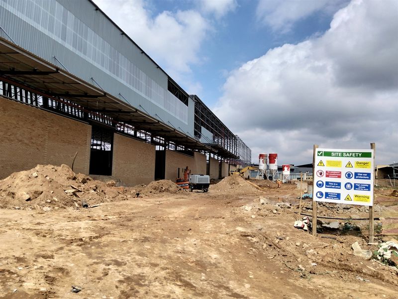 Exterior view of an industrial property currently under construction, featuring a large steel-framed structure with brick walls and on-site silos.