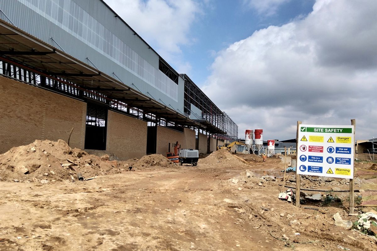Exterior view of an industrial property currently under construction, featuring a large steel-framed structure with brick walls and on-site silos.