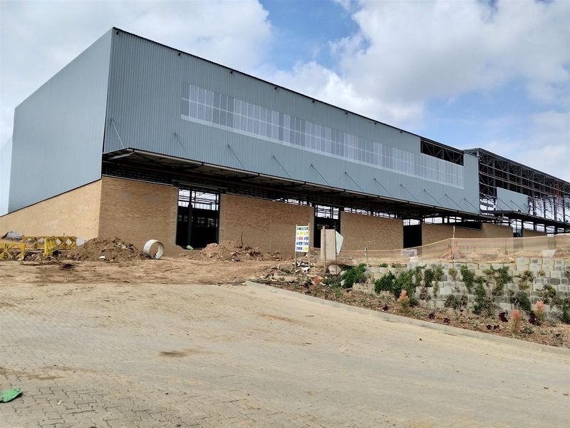 Exterior view of an industrial warehouse facility currently under construction, featuring a steel frame, brick base, and corrugated metal upper cladding.