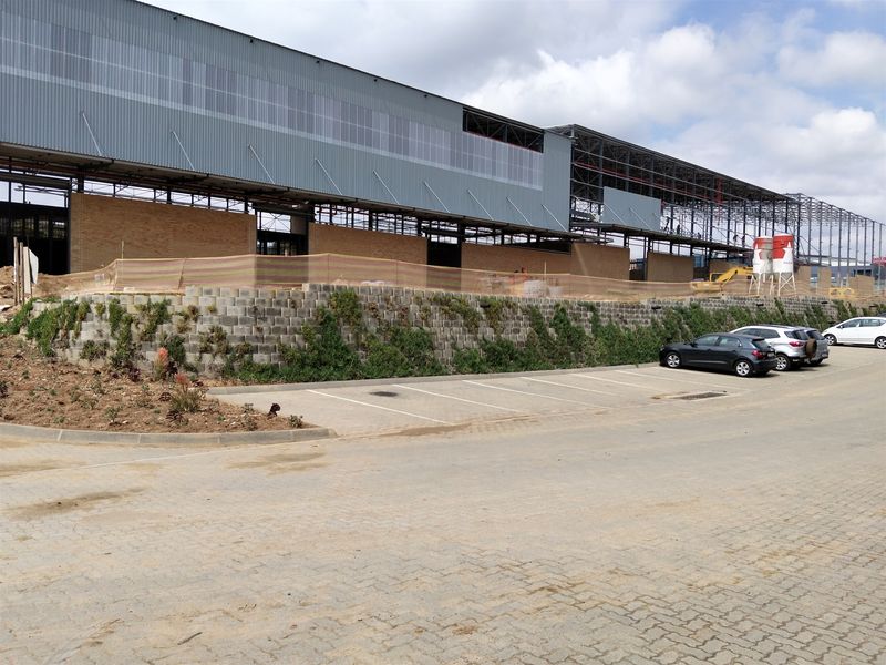 Exterior view of an industrial property under construction, featuring a large steel frame structure, metal cladding, brickwork, and a paved parking area.