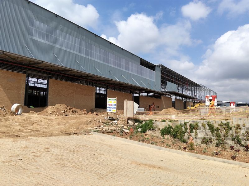 Exterior view of an industrial warehouse facility currently under construction, featuring brick masonry walls, steel framing, and corrugated metal cladding.