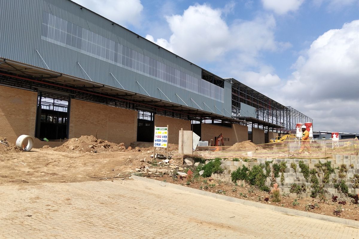 Exterior view of an industrial warehouse facility currently under construction, featuring brick masonry walls, steel framing, and corrugated metal cladding.